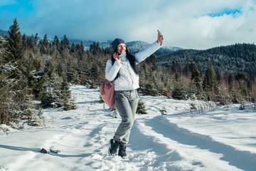 A girl is taking pictures of a mountain landscape. Beautiful mountain lake in winter. Snowy mountains and trees. Outdoor activities. Red jacket and backpack.