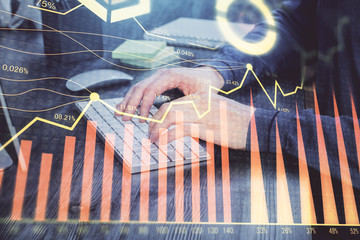 Stock graph with businessman typing on computer in office on background. Concept of analysis. Double exposure.
