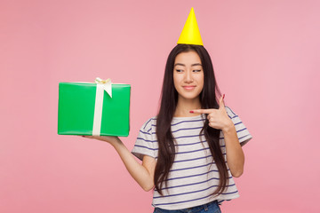 Portrait of pretty girl with party cone on head pointing at gift box, showing great birthday present, offering anniversary bonus, holiday celebration. indoor studio shot isolated on pink background