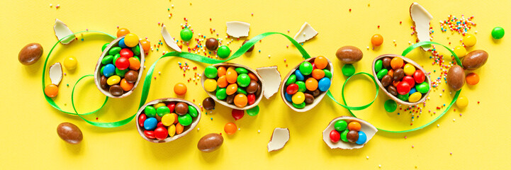 Chocolate Easter eggs and colorful candies on yellow paper background. flat lay, top view, overhead, template, mockup
