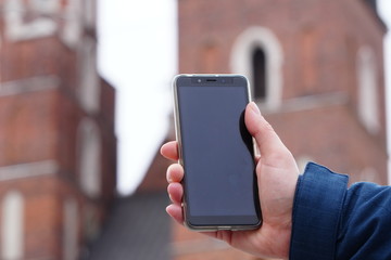 Hand of tourist holding mobile smartphone with black screen on the background of an old house, photographing sights or architecture. Journeys or Travel concepts and technology