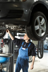 Handsome mechanic in uniform is working in auto service with lifted vehicle. Car repair and maintenance. Oil change