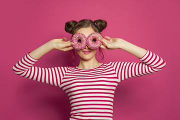 Smiling woman holding donut on colorful pink background, diet concept