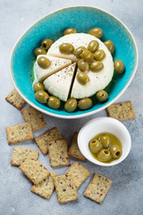 Green olives and soft cheese with black pepper, olive oil and crackers. Vertical shot on a light-blue stone surface