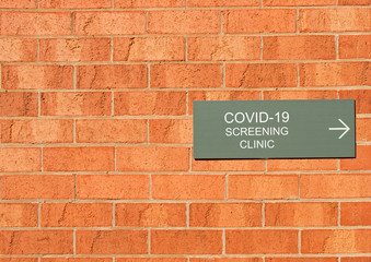 a COVID-19 Screening Clinic sign on a red brick wall