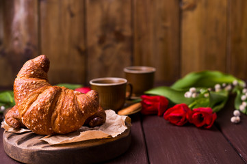 croissant and coffee. Fresh italian pastries and aromatic coffee on a wooden table and red tulips. Rustic style photo .