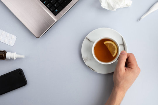 Man working from home during quarantine. Coronavirus concept. Laptop, mobile, cup of tea with lemon and items for treatment and prevention on gray background. Top view, flat lay, copy space
