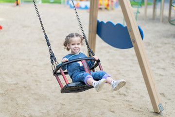 Little Caucasian girl riding swing at playground sunny summer day.