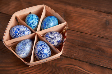 Blue cosmos chicken eggs lie in round wooden basket which stands on a dark wooden table.