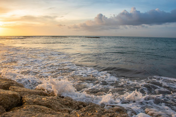 Sunshine from horizon on the stones of the seashore with waves and white bubbles during the summer time in Bali