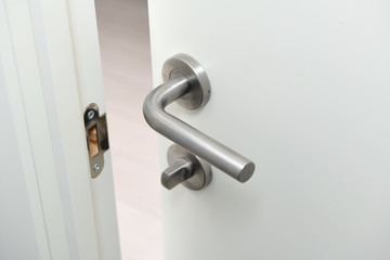 Detail of a metallic knob on white door horizontal.Stainless steel handle on a white wooden...
