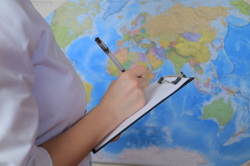 Woman doctor is writing notes on paper near global map
