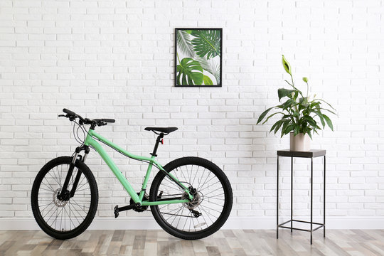 Modern green bicycle near white brick wall in stylish room interior