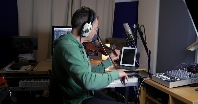 Violinist recording violin part in recording studio onto a DAW (Digital Audio Workstation) and then editing the audio.  A home recording studio setup ideal for singer songwriters creating new music.