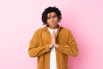 Young African American man with corduroy jacket over isolated pink background keeps palm together. Person asks for something