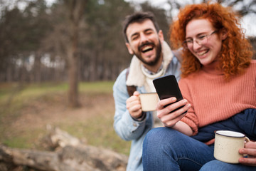 Young couple using modern technology. Smiling couple drinking coffee in the park. the couple use a nice sunny spring day to party in the park.