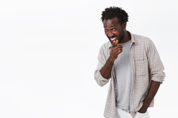 Cheerful, funny and cheeky young african-american bearded man in casual clothes, pointing finger...