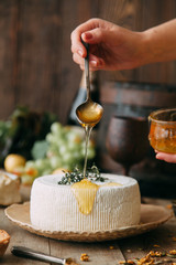  A large white round cheese on a plate. Curd cheese is watered with honey. The chef's hands prepare cheese.
