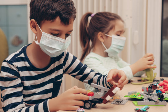 Cute children boy and girl in medical mask is sitting at home in quarantine. Сhildren play constructor after disinfection hands. Entertainment for the children during quarantine. Self isolation 