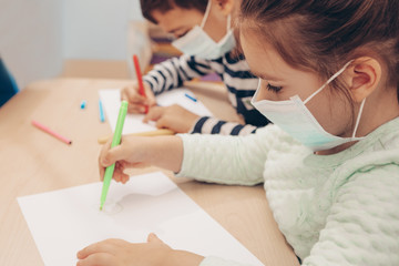 Cute children boy and girl in medical mask is sitting at home in quarantine. Entertainment for the children during quarantine - drawing. Self isolation. children draw and play constructor after hands