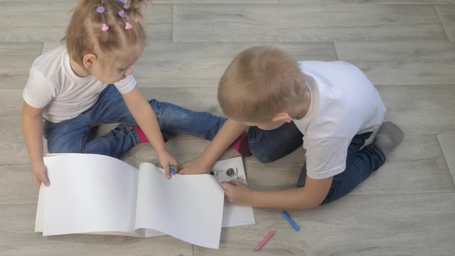 happy family brother and sister teamwork lifestyle concept. little boy and girl draw on floor in a sketchbook. brother and sister in the room draw with crayons