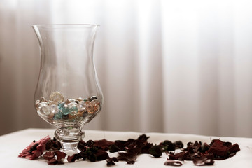 Glass vase in the shape of a wineglass, decorative stones and dry fragrant flowers on the table, light blurred background