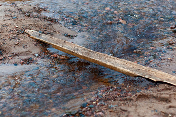 Homemade bridge over a small stream on the sandy shore of the bay, clear water and small pebbles on a spring cloudy day