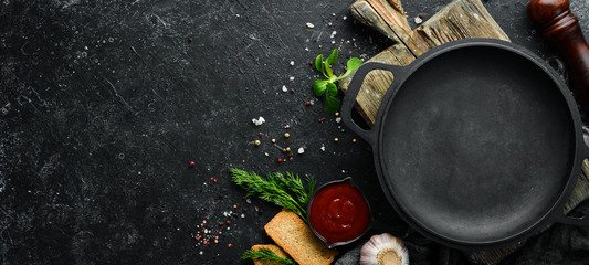 Black frying pan on stone background with vegetables and spices. Top view. Free space for your...