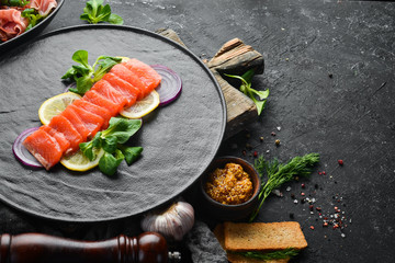 Salted fish salmon with lemon and onions on a black plate. Top view. Free space for your text. Rustic style.