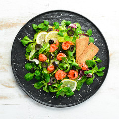Fresh salad with salmon and olives in black plate. Top view. Free space for your text. Rustic style.