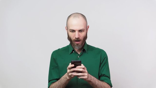 Handsome bearded man surprized and shocked using mobile phone over white background. People sincere emotions, lifestyle concept. Cell phone user.