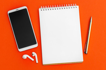 Notepad with smartphone and pen on orange background. Top view. Copy Space.