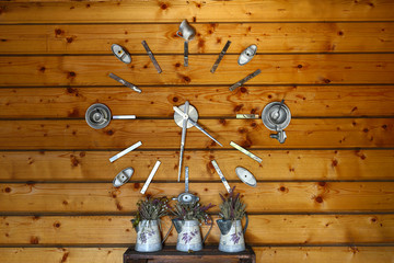 Decorative clock in a street cafe. Metal arrows and shapes of kitchen utensils on wooden wall. Street decor of lavender utensils.
