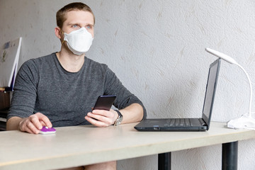 Fototapeta na wymiar young man in protective medical mask works at a table at home, home quarantine during a pandemic
