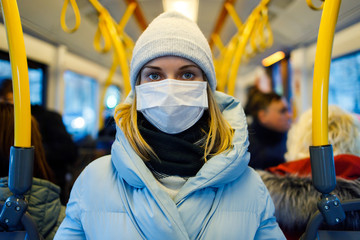 Girl in medical mask standing in bus lounge next to yellow handrails in afternoon.