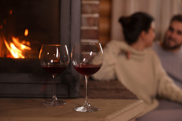 Lovely couple near fireplace at home, focus on glasses with wine. Winter vacation