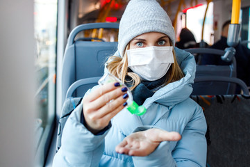 Obraz na płótnie Canvas Blonde in medical mask looking at side disinfects her hands with tool while sitting on bus near window