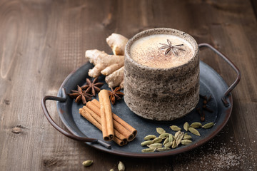 Masala tea in a ceramic cup with cardamom, star anise, cinnamon and ginger on a wooden background. Antiviral drink for immunity. Top view, place for text.