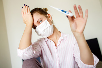 Close-up of young female in medical mask with thermometer in her hand . Coronavirus epidemic