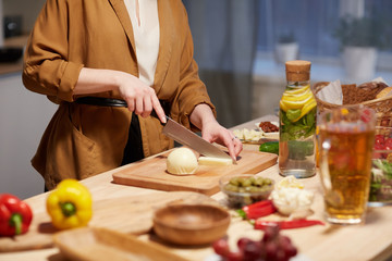 Close-up of woman cutting cheese on cutting board with kitchen knife at the kitchen table