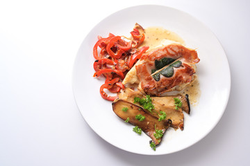 Roasted chicken saltimbocca with air-dried ham and sage leaves on a plate with red bell peppers and king oyster mushrooms, white background with copy space, high angle view from above