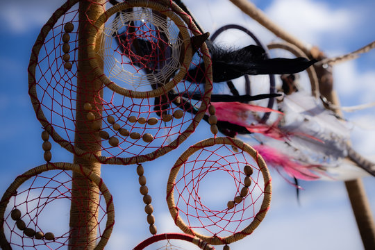 Pendant of the dream catcher on the nature against a background of blue summer sky with black, white and pink feathers