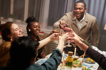 Group of happy young people toasting with wineglasses with wine and celebrating the holiday during dinner at home