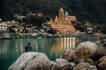 Man is sitting at the river and looking at the temple in Rishikesh, India