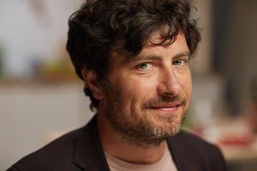 Fototapeta premium Portrait of mature man with stubble smiling at camera while visiting party