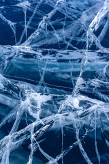 Large and small cracks in the ice. Blue transparent thick ice. Vertical.