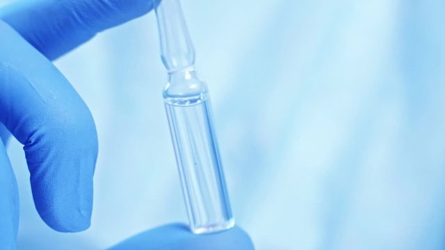 Drug manufacturing. Pharmaceutical science. Technician hand in blue glove holding ampoule.