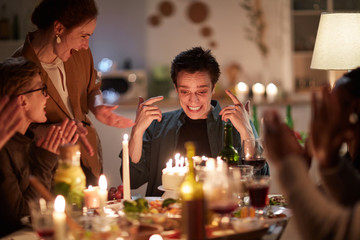 Young man happy with his birthday cake with candles while sitting at the table with his friends at home