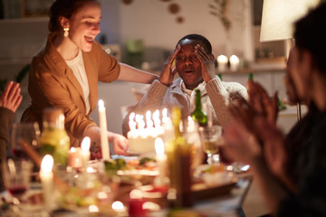 African young man happy with birthday cake with candles while celebrating his birthday together with friends at home