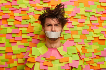 Depressed melancholic man with taped mouth, forced keep silence and not speak, looks sadly at...